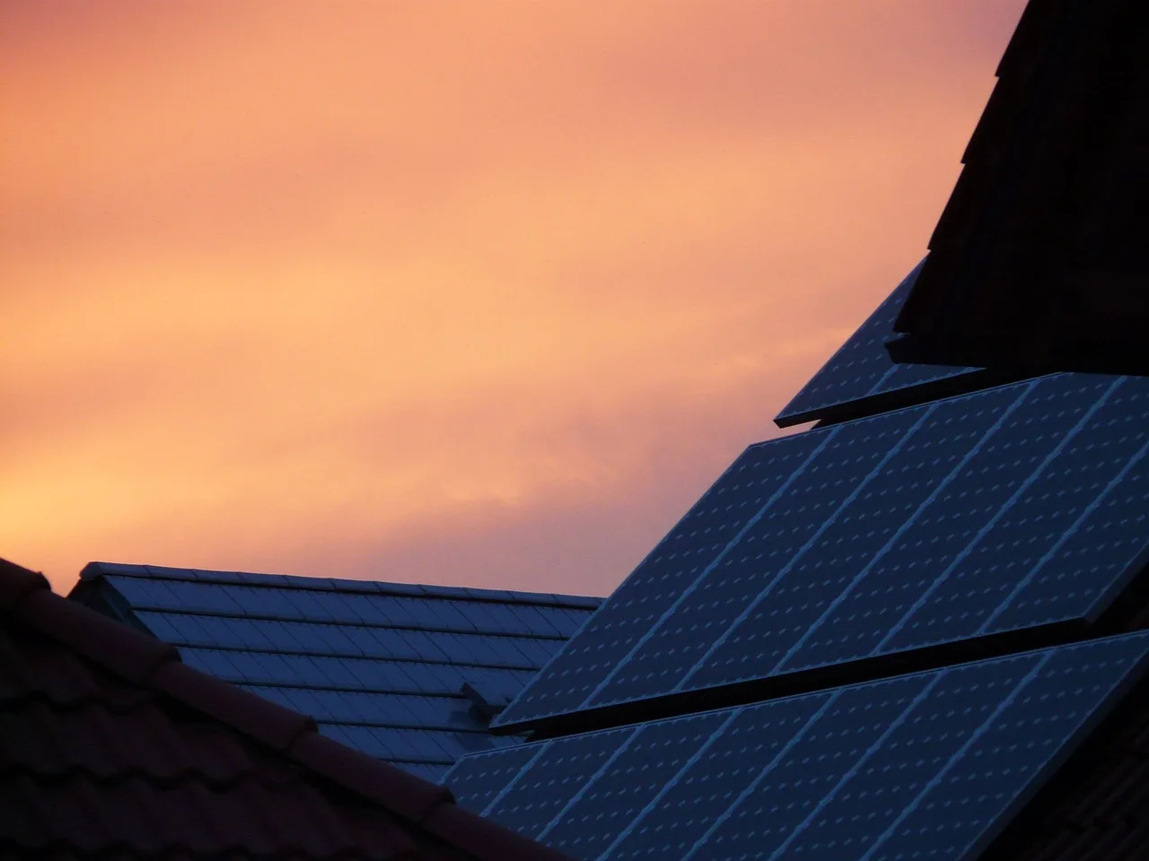 Solarmodule auf einem Dach vor rot gefärbtem Abendhimmel.