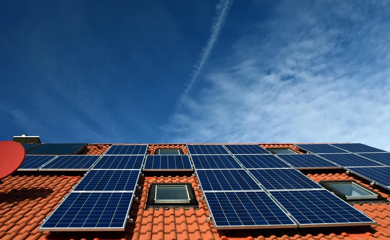Solarmodule auf einem roten Ziegeldach zwischen zwei Dachfenstern.