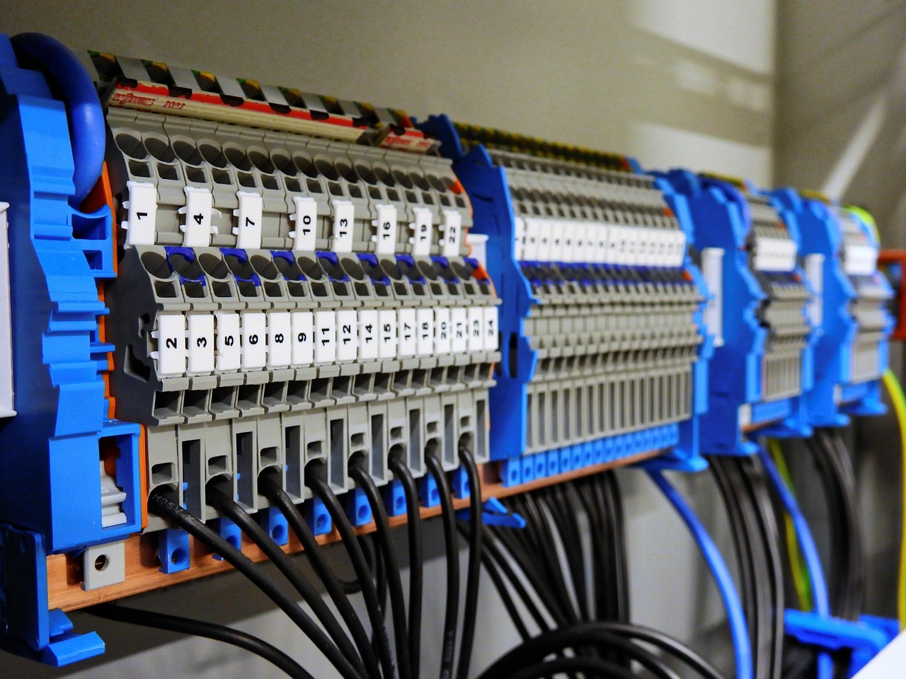 Nummerierte Reihenklemmen auf Hutschienen in einem geöffneten Elektroverteiler mit schwarzen Adern.