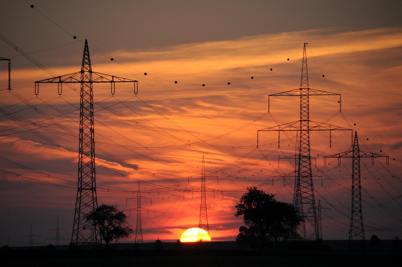 Hochspannungsmasten und Freileitungen als Silhouette vor einem Abendhimmel bei Sonnenuntergang