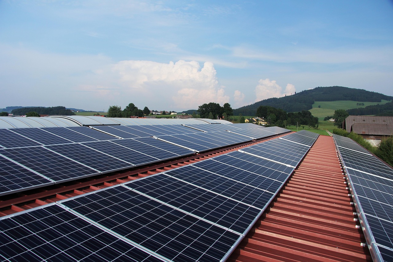 Photovoltaikmodule in mehreren Reihen auf einem roten Blechdach, im Hintergrund eine hügelige Landschaft