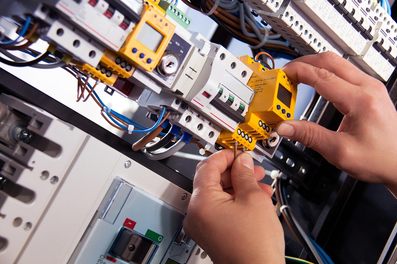 Elektrofachkraft arbeitet mit beiden Haenden an einer offenen elektrischen Verteilung mit Sicherungen und Kabeln
